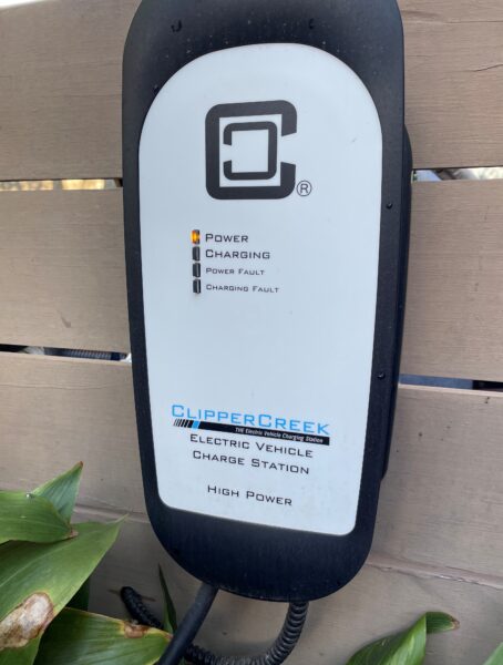 Electric vehicle charging station with ClipperCreek logo, showing Power indicator lit and surrounded by green leaves.