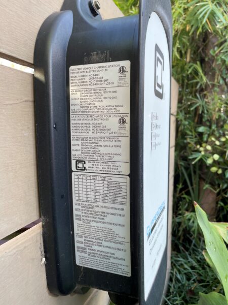 Close-up of an electric vehicle charging station with specifications and warnings visible on its side panel.